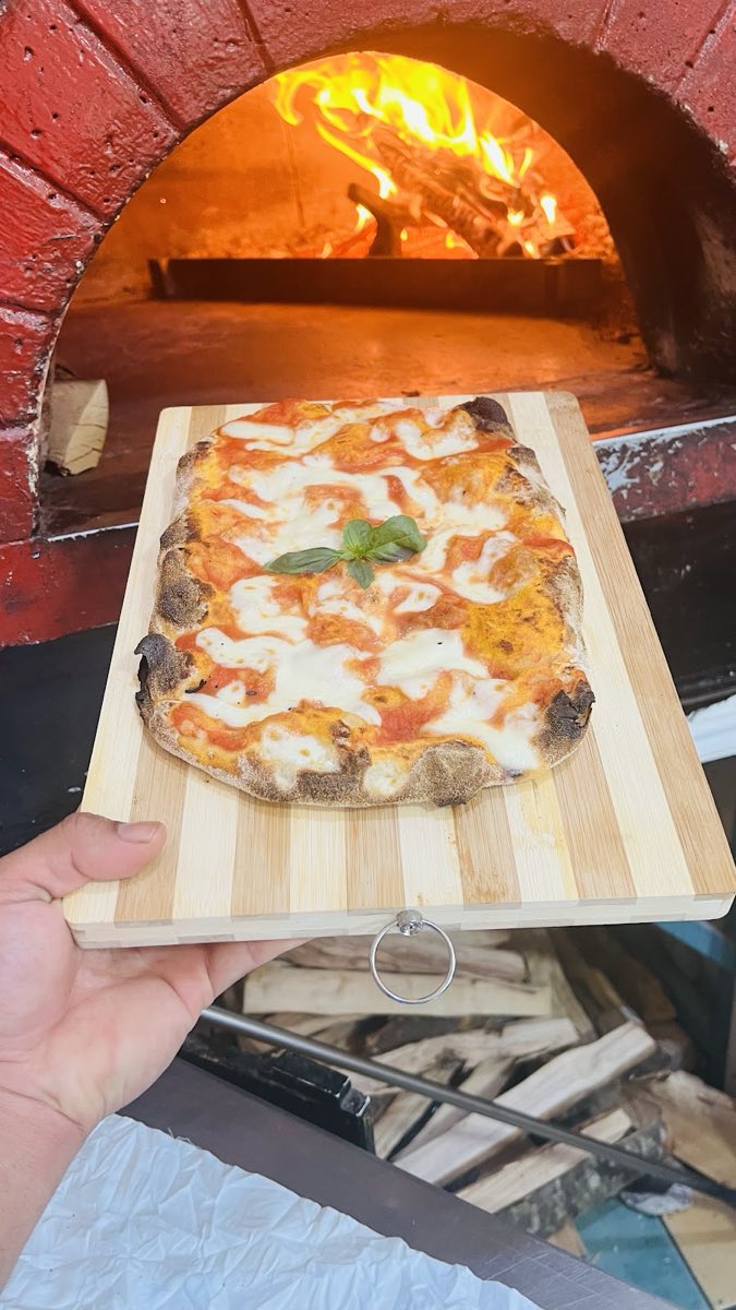 Pinsa margherita appena sfornata davanti al forno a legna acceso